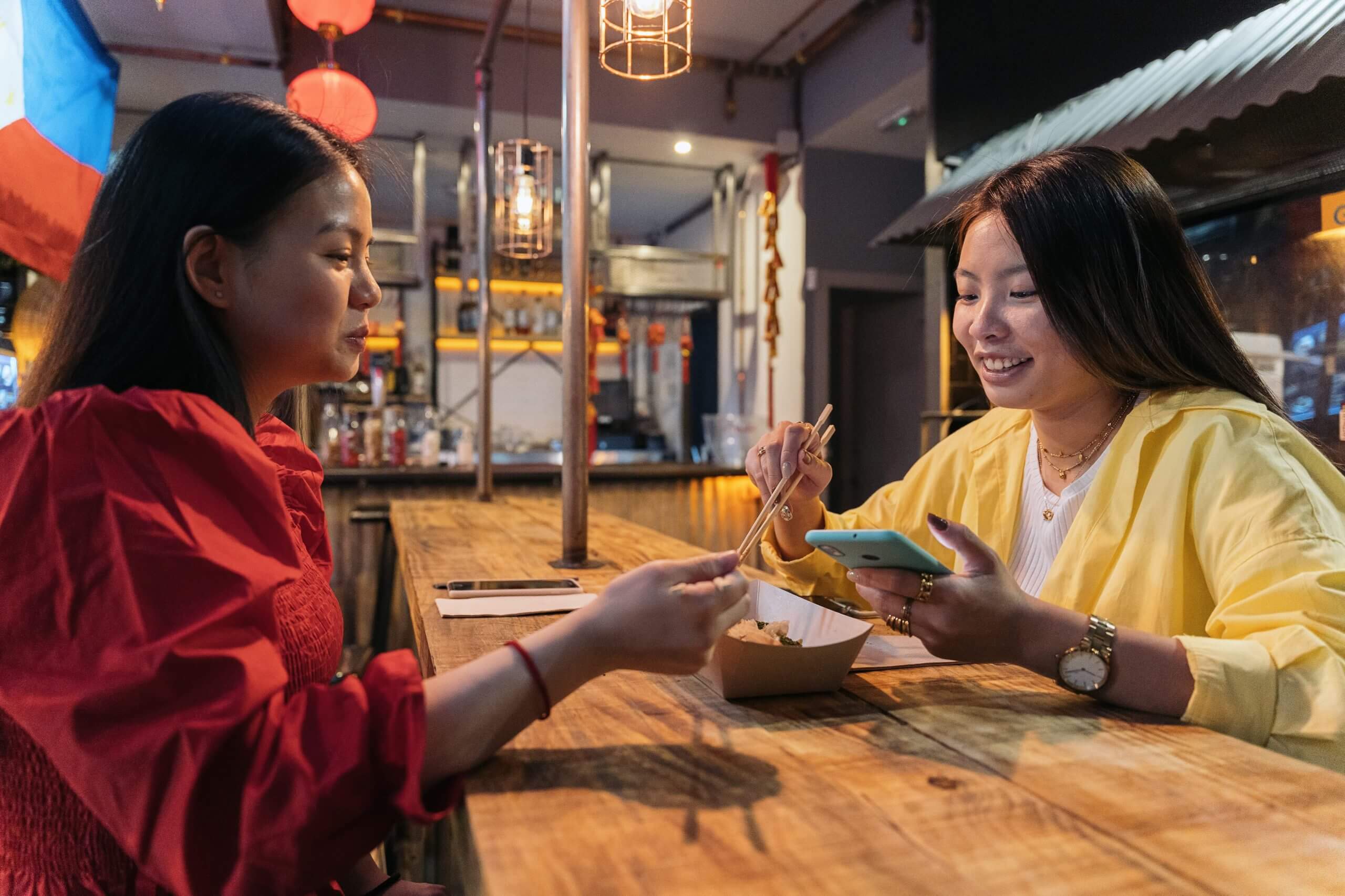 Happy asian female friends sitting in chinese restaurant eating and talking.